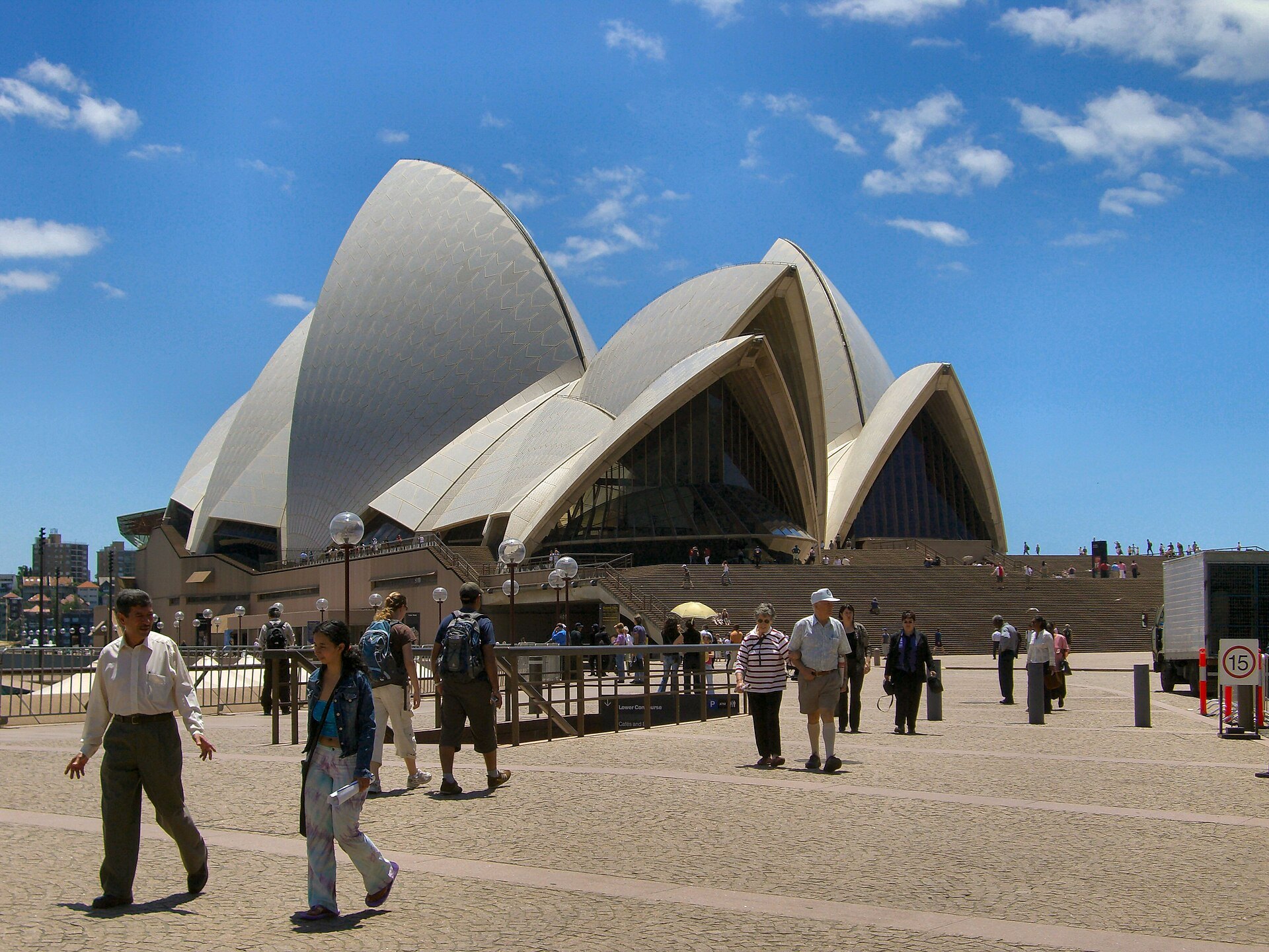 The Opera House forecourt with people walking across it beneath the shells