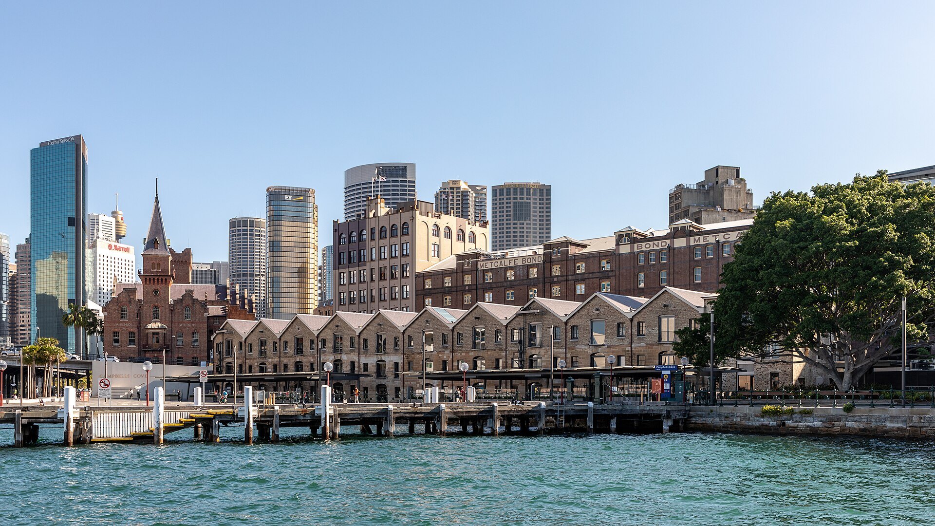 The Rocks seen from the water, wharves and warehouses below the city towers